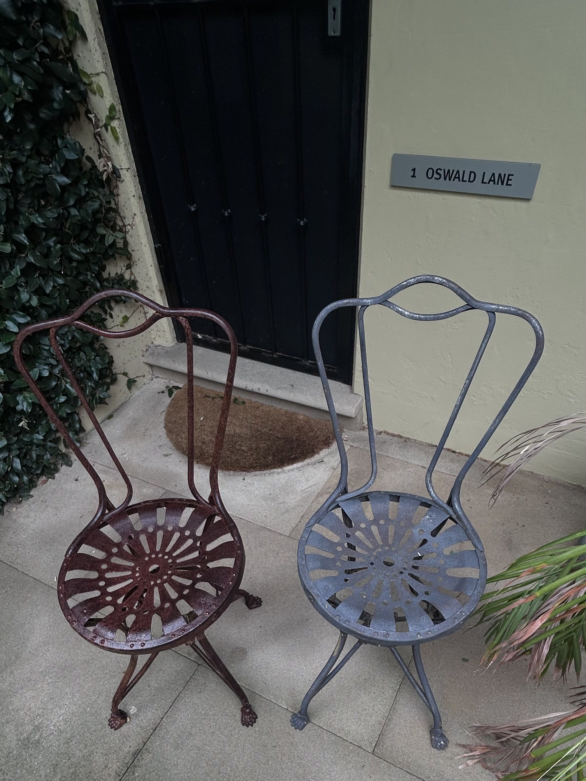 Two vintage cast-iron tractor-seat garden chairs at a doorway — left chair before laser cleaning (rusted), right chair after (cleaned, original casting detail preserved)
